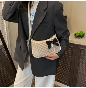 Detail of cream shoulder bag with M monogram, black bow, and pearl charm detail
