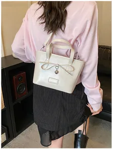 Close-up of beige glossy tote bag featuring a bow, heart pendant, and fashion logo plate