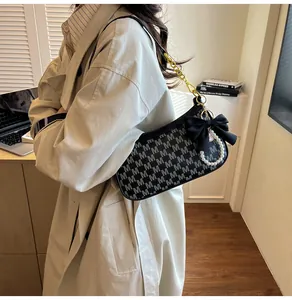 Detail of black armpit bag with M-pattern, bow decoration and pearl charm accessory