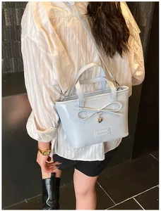 Close-up of light blue fashion tote bag with bow detail and heart pendant on a model
