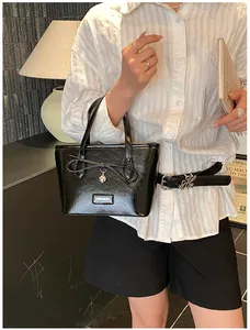 Close-up of black glossy tote bag with bow detail and heart pendant with FASHION metal logo
