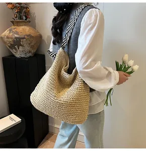 Detail of a large beige straw woven tote bag featuring black and white striped ribbon accent