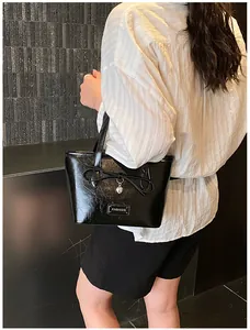 Close-up of black tote bag featuring a bow, heart pendant, and Fashion label