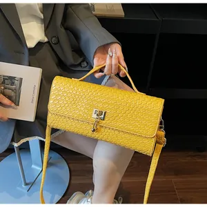 Dettaglio di borsa gialla in pelle goffrata coccodrillo con chiusura a scatto e ciondoli