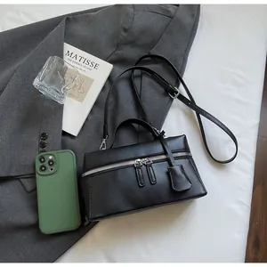 Top view of a black leather handbag with dual zippers, shoulder strap, and a phone for scale