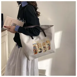 Close-up of a large canvas tote bag featuring an Egyptian Anubis art print and leather handles