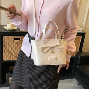 Cream tote bag with bow detail and heart charm, shown in a lifestyle street style setting