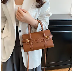 Sac bandoulière en cuir grainé marron porté par un mannequin en blazer blanc