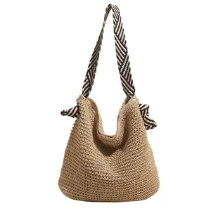 Handwoven straw tote bag with black and white striped shoulder strap for beach vacation
