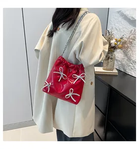 Modella che indossa una borsa a secchiello in vernice rossa con fiocchi e catena d'argento
