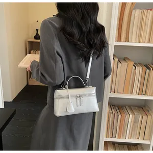 Silver glossy leather handbag with double zipper and adjustable strap on a grey blazer