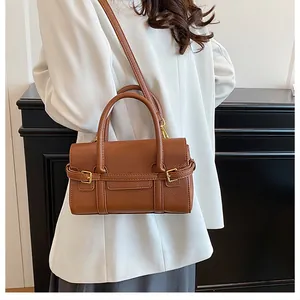 Sac à main marron en cuir avec boucle dorée porté par un mannequin en blazer blanc
