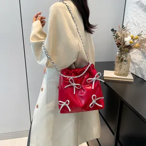 Borsa a secchiello rossa lucida con fiocchi argentati e catena su un trench beige