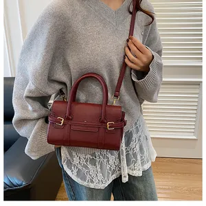 Détail d'un sac à main en cuir bordeaux à grain avec boucle dorée par un modèle
