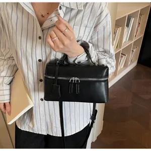 Detail view of a black leather box handbag with silver hardware held by a model