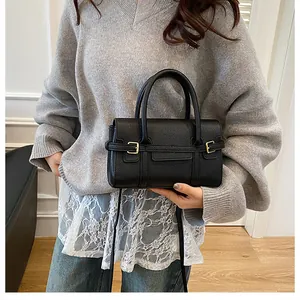 Gros plan du sac à main en cuir grainé noir avec boucles dorées porté par un mannequin