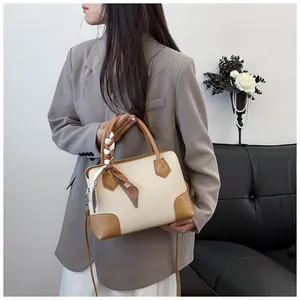 Détail du sac Boston tissé avec finitions en cuir et foulard floral sur un canapé noir
