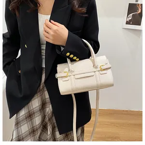 Détail d'un sac à main beige texture litchi avec boucles dorées porté avec une tenue chic