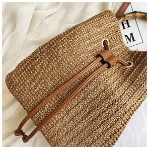 Detail of woven straw bucket bag with bamboo handle, brown drawstring and metal eyelets