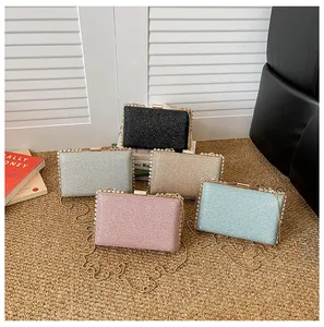 Detail of glitter clutch bags in five colors with gold chains on a textured rug