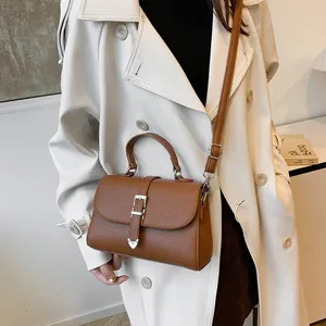 Sac à main marron en cuir grainé avec boucle argentée porté sur un trench-coat beige