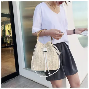 Detail of beige straw bucket bag featuring bamboo handle and white drawstring closure