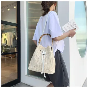 Detail of cream woven bucket bag with bamboo handle and adjustable leather strap