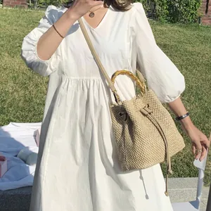 Natural straw bucket bag featuring bamboo handles and leather strap on a sunny lawn