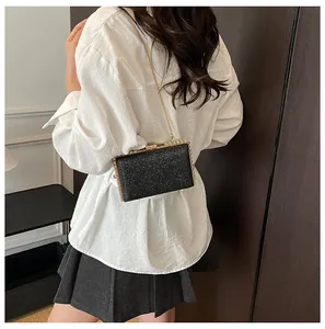 Detailed view of black glitter box bag with gold chain strap worn by a model