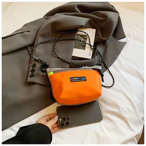 Detailansicht der orangefarbenen Nylon-Umhängetasche mit Etikett und gewebtem Schultergurt