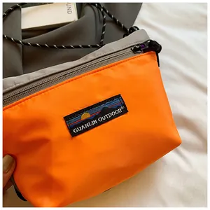Detailansicht der orangefarbenen Nylon-Umhängetasche mit Markenlogo und grauem Reißverschluss