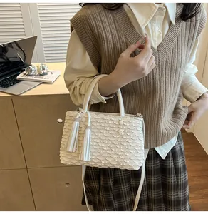 Detail of white pleated tote bag with fish scale texture and twin tassel charms