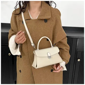 Détail du sac à main beige texturé avec fermoir ovale en métal porté sur un manteau en laine