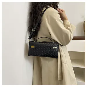 Close-up of black woven leather handbag with gold metal accents worn by a model