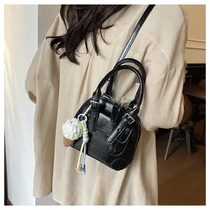 Model showing a black glossy shell-shaped handbag with adjustable strap and charm