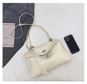 Detail view of beige crocodile embossed leather handbag with silver twist lock and slim strap