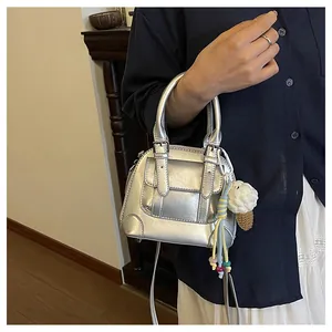Detail of silver metallic shell bag featuring buckle pockets and a knit ice cream charm