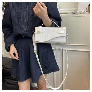 Detail of white woven texture handbag with gold buckle held by a model in denim outfit