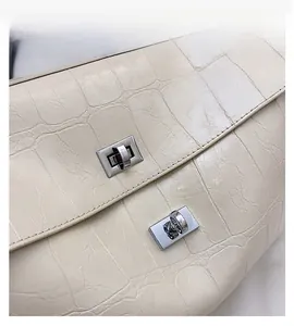 Detail of cream crocodile embossed handbag featuring dual silver twist-lock hardware