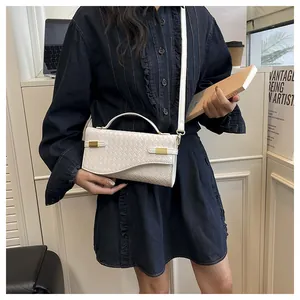 Detail of white woven texture handbag with matte gold clasp held by a model in denim