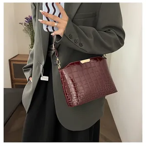 Detail of dark red crocodile embossed crossbody bag with glossy finish and gold metal trim
