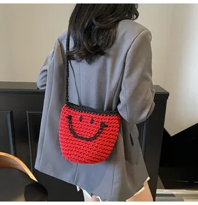 Model wearing a red hand-knitted mini bucket bag with a black smile face and strap