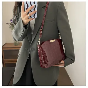 Detail of burgundy crocodile pattern shoulder bag with polished finish and gold hardware