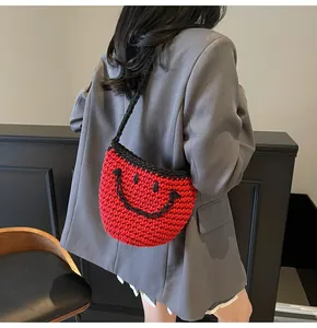 Detail of red and black hand-woven bucket bag with smiley face and knit shoulder strap