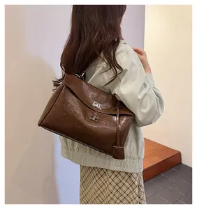 Brown faux crocodile leather bag with silver metal clasp worn by a model in casual attire