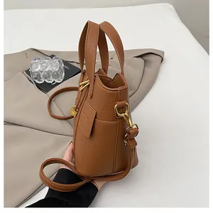 Détail du cuir marron à grain de litchi avec des ferrures dorées sur le sac seau