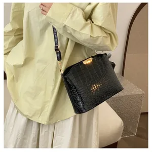 Close-up of black crocodile pattern leather handbag with gold metal clasp on a model