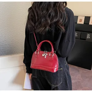 Sac à main rouge verni avec breloques cœur en argent porté à l'épaule par un mannequin