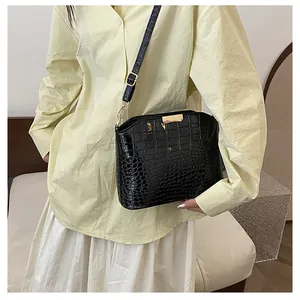 Detail of glossy black crocodile pattern crossbody bag with gold metallic buckle on model