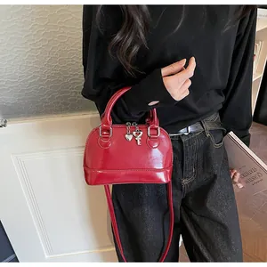 Détail du sac à main rouge en forme de coquille avec finition brillante et breloque cœur